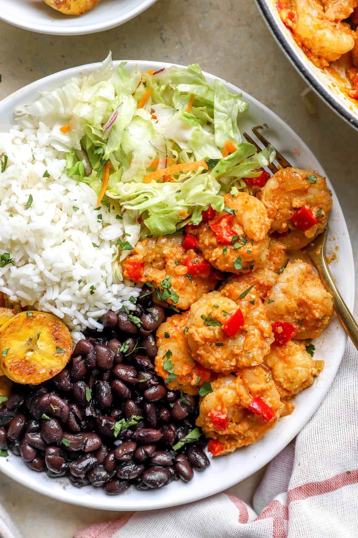 A bowl of Costa Rica skillet garlic shrimp with black beans, plantains, rice, and salad, a fork on the side.