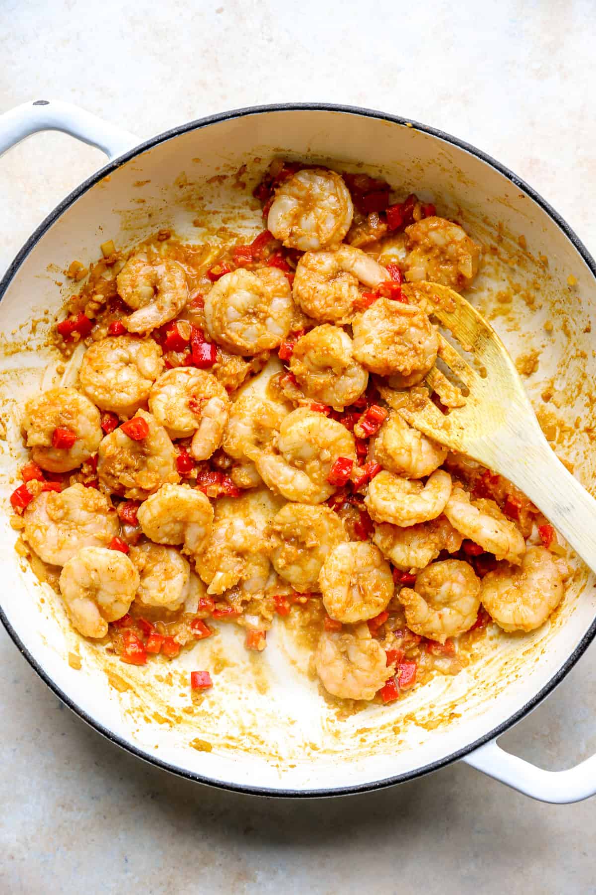 Marinated garlic shrimp, peppers, and onions in a skillet, a wooden spoon sticking out.
