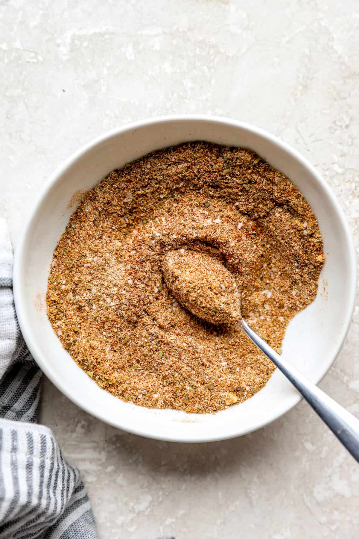 A bowl of homemade Sazón seasoning with a spoon sticking out.