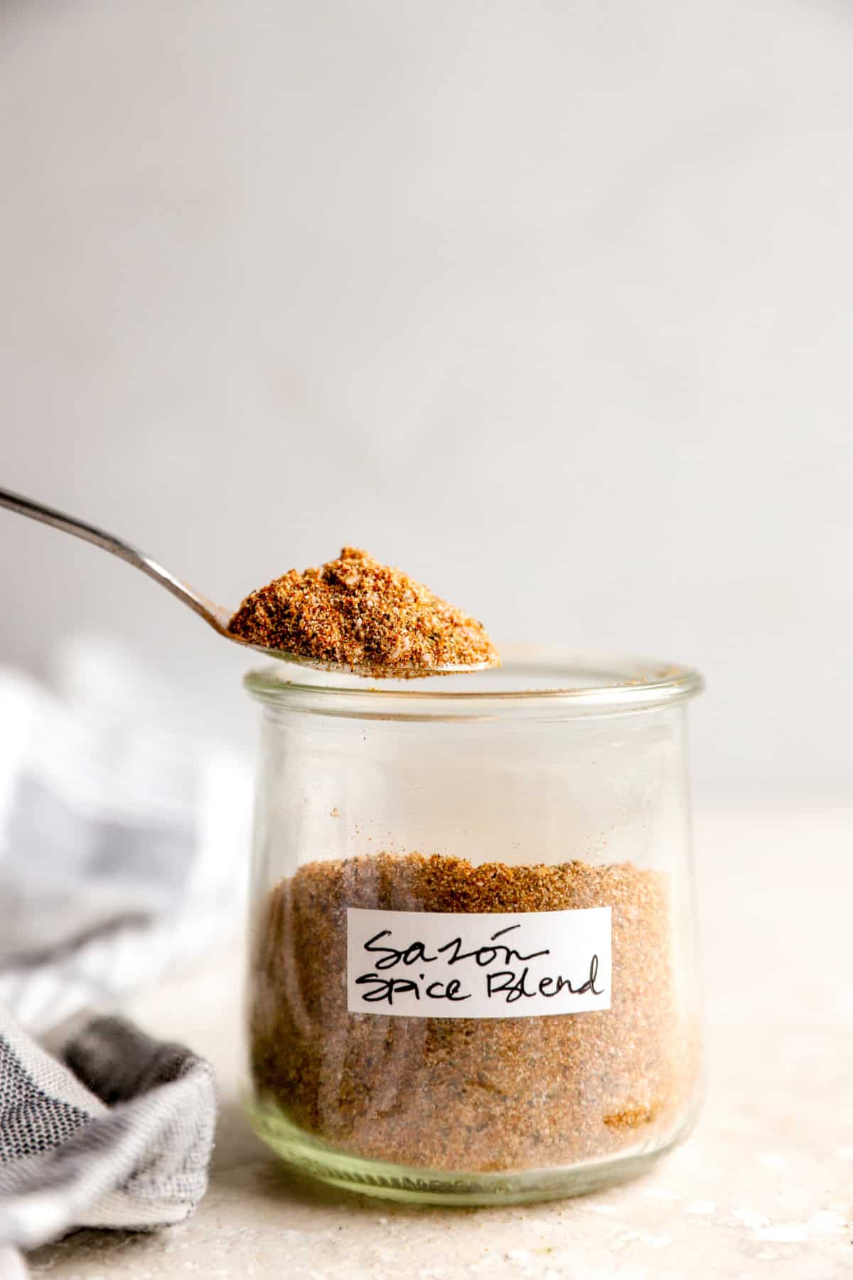A spoon lifting a spoonful of seasoning from a jar of homemade Sazón seasoning.