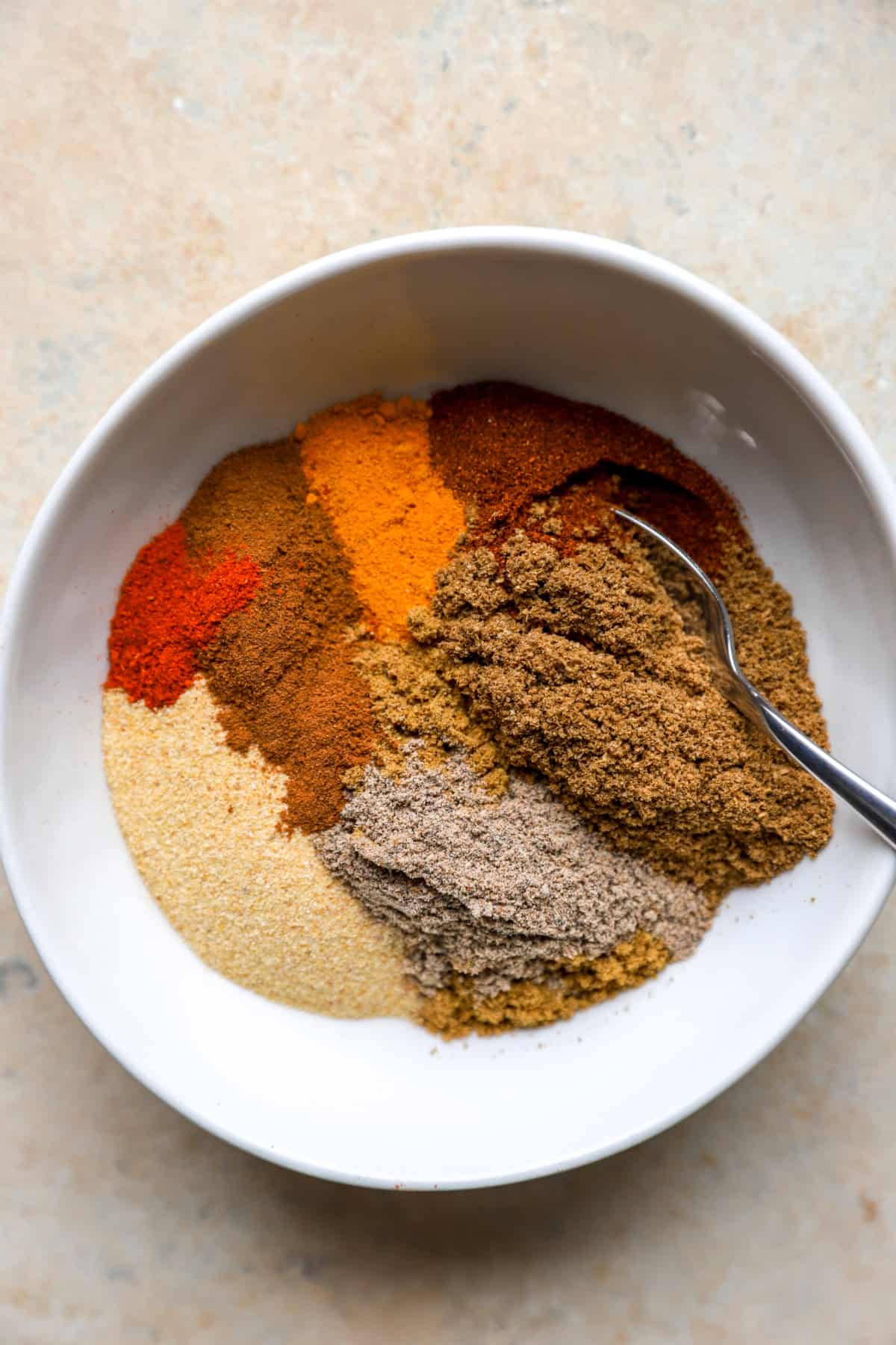 A bowl of seasonings with a spoon sticking out.
