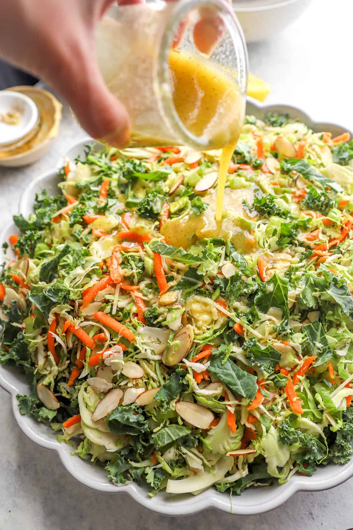 Lemon Dijon vinaigrette being poured over a bowl of Brussels sprouts and kale slaw.
