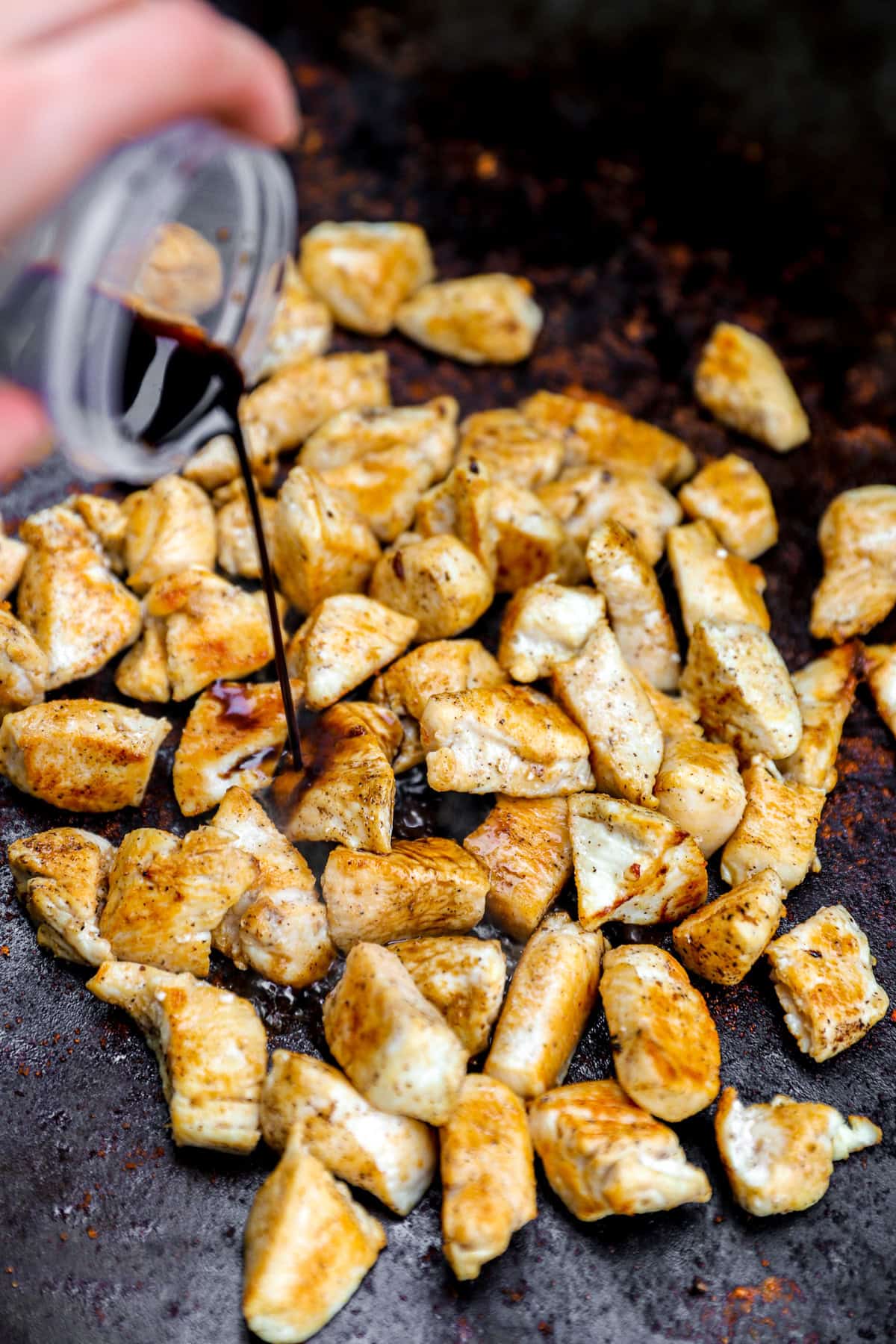 Coconut aminos being poured over chicken pieces in a skillet.