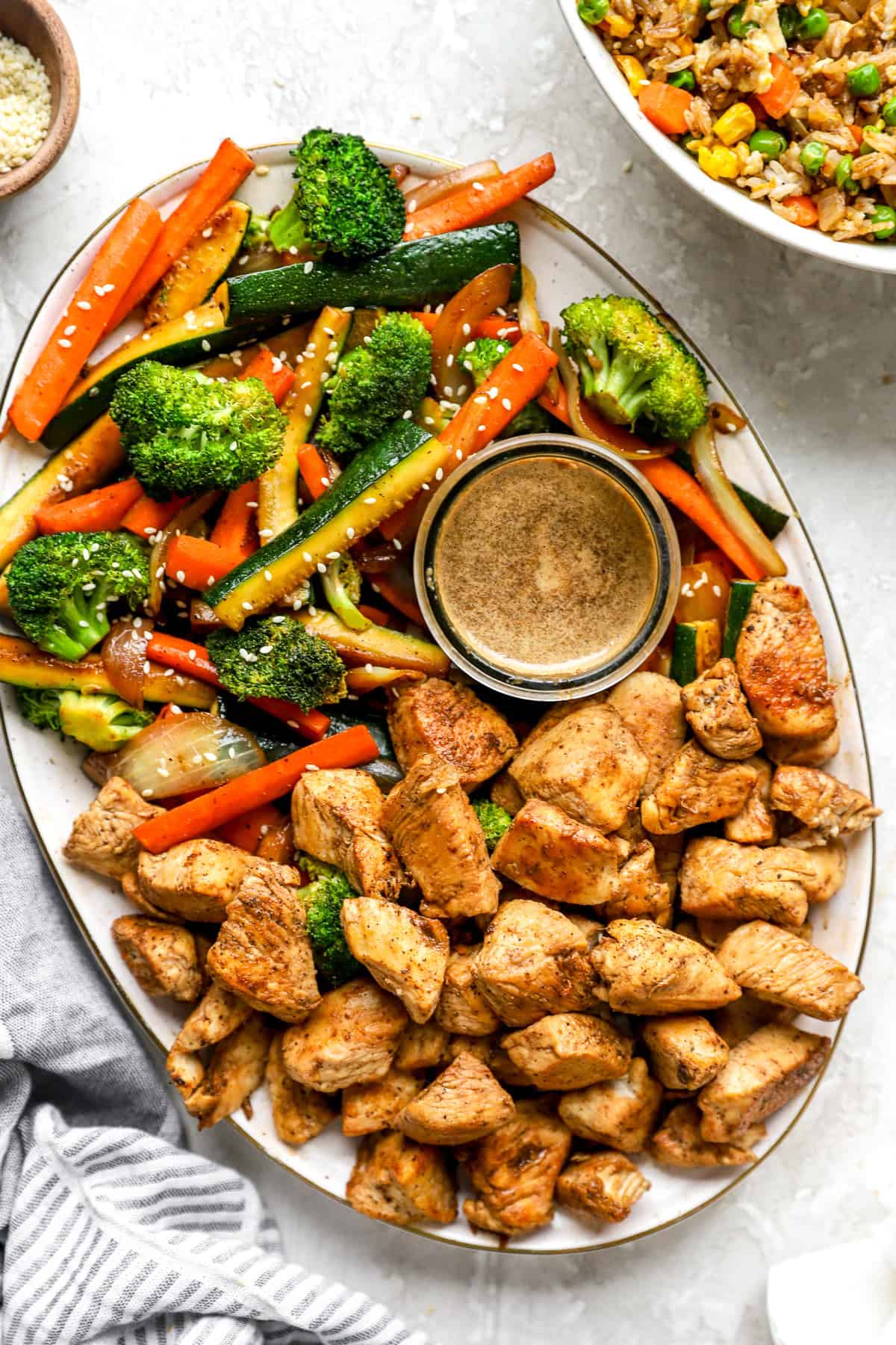 A platter of hibachi chicken and vegetables with a bowl of hibachi ginger sauce.