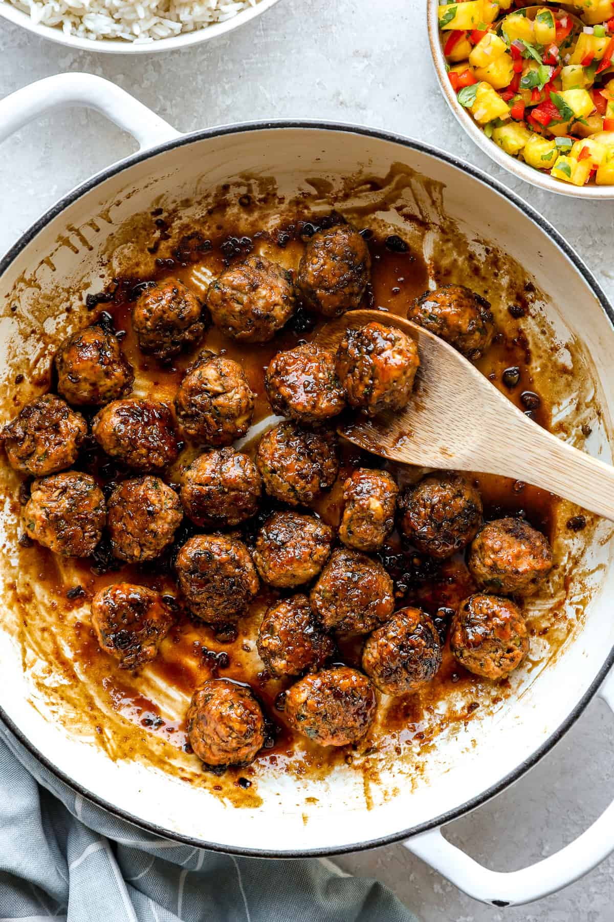 Honey garlic chicken meatballs being tossed with glaze in a skillet.
