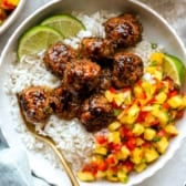 A bowl of honey garlic chicken meatballs with pineapple salsa, coconut rice, and limes.