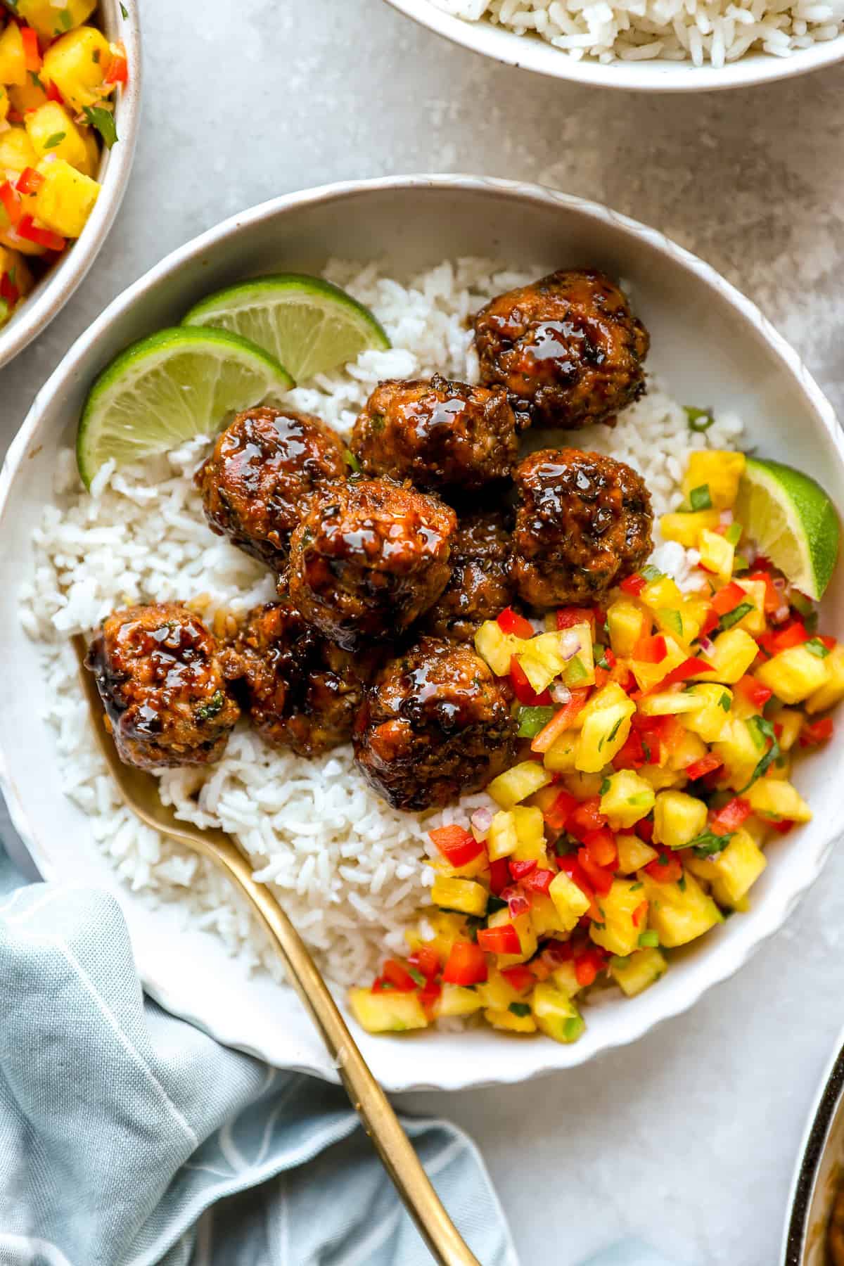 A bowl of honey garlic chicken meatballs with pineapple salsa, coconut rice, and limes.
