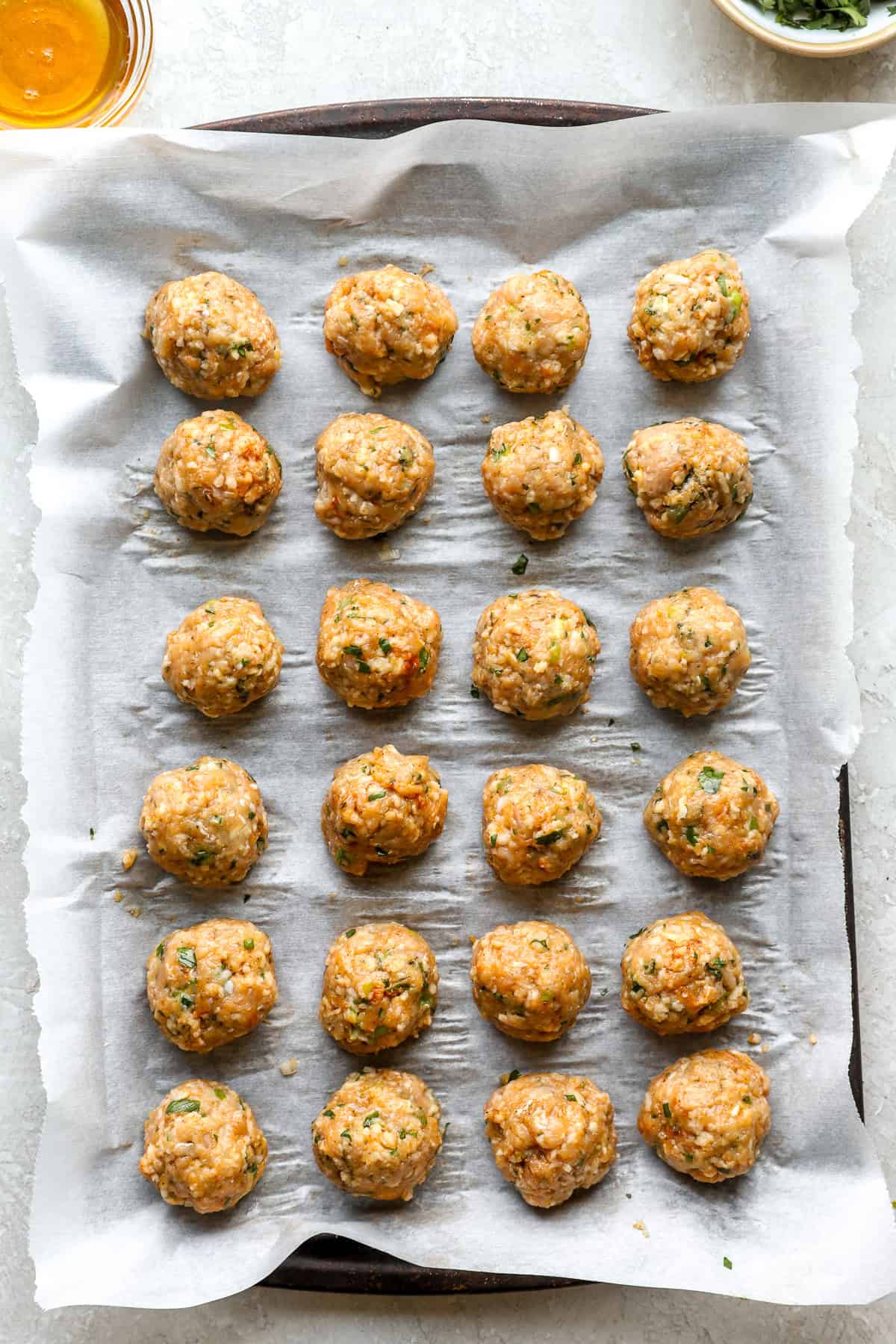Raw honey garlic chicken meatballs on an aluminum foil-lined baking sheet.