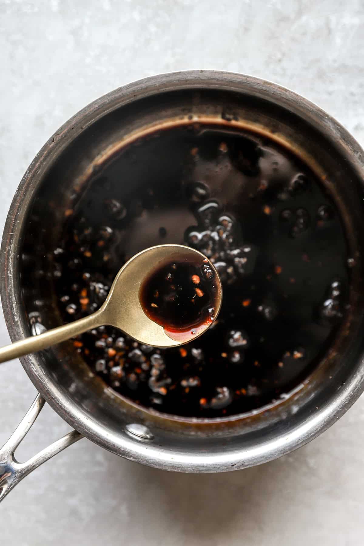 Honey garlic glaze in a pot, a spoon lifting a scoop.