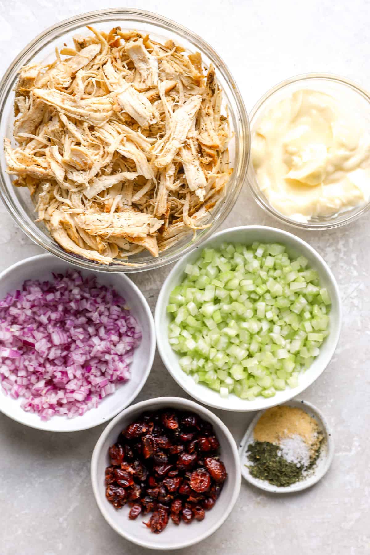 Bowls of shredded chicken, mayo, diced celery, diced red onion, cranberries, and seasonings.