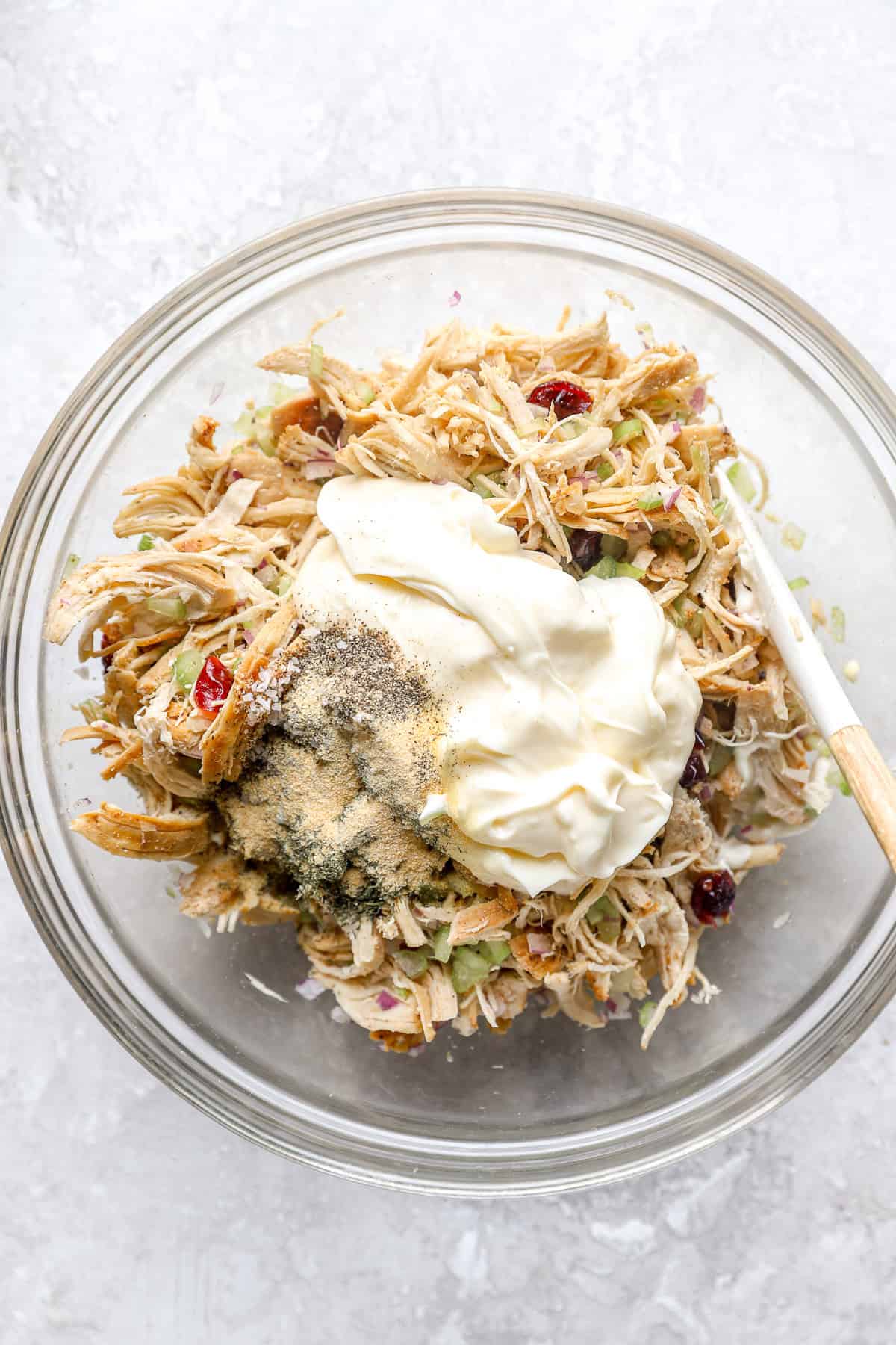 A bowl of shredded chicken, diced celery, diced red onions, and cranberries topped with mayo and spices.