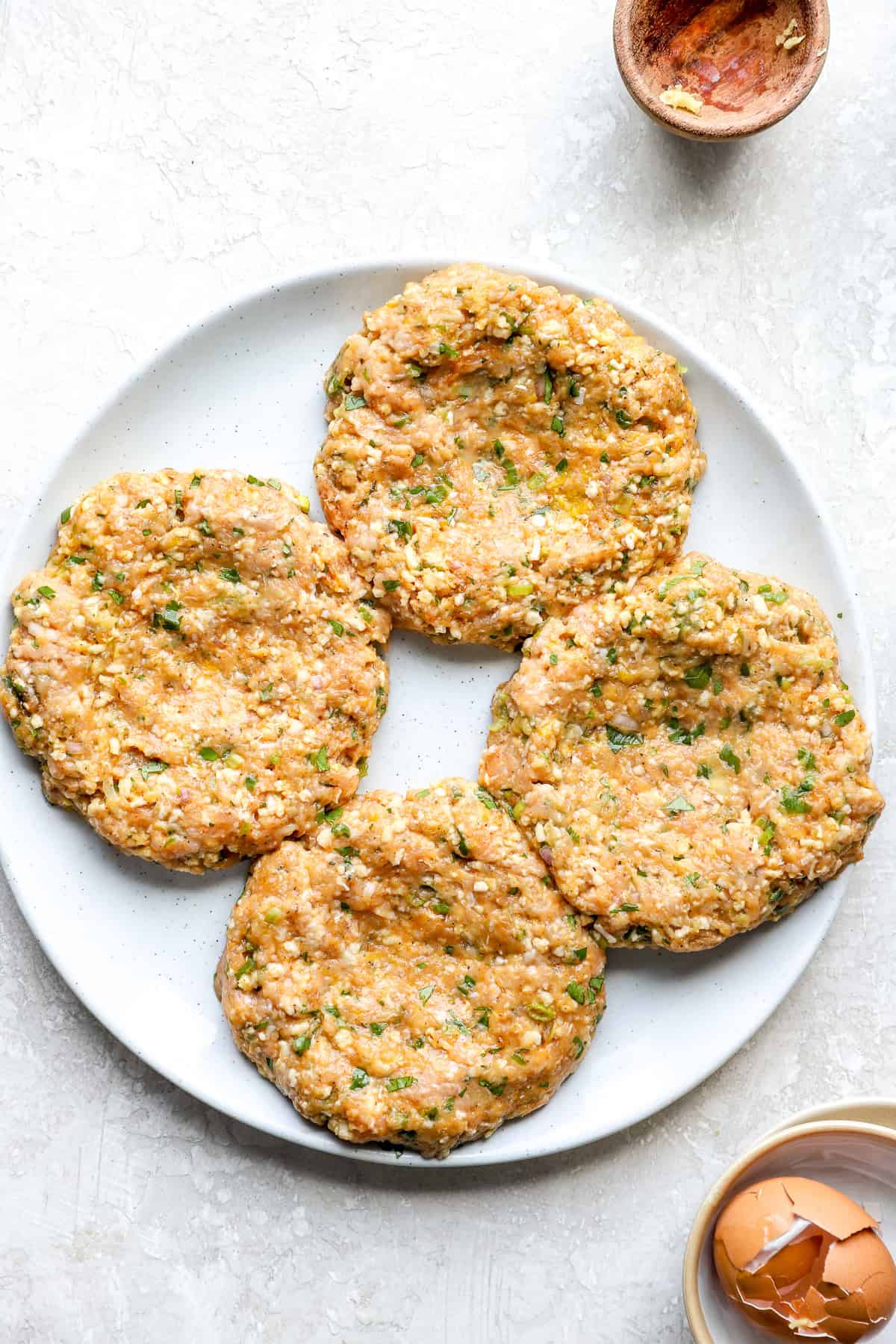 Four raw ground chicken burgers on a plate.