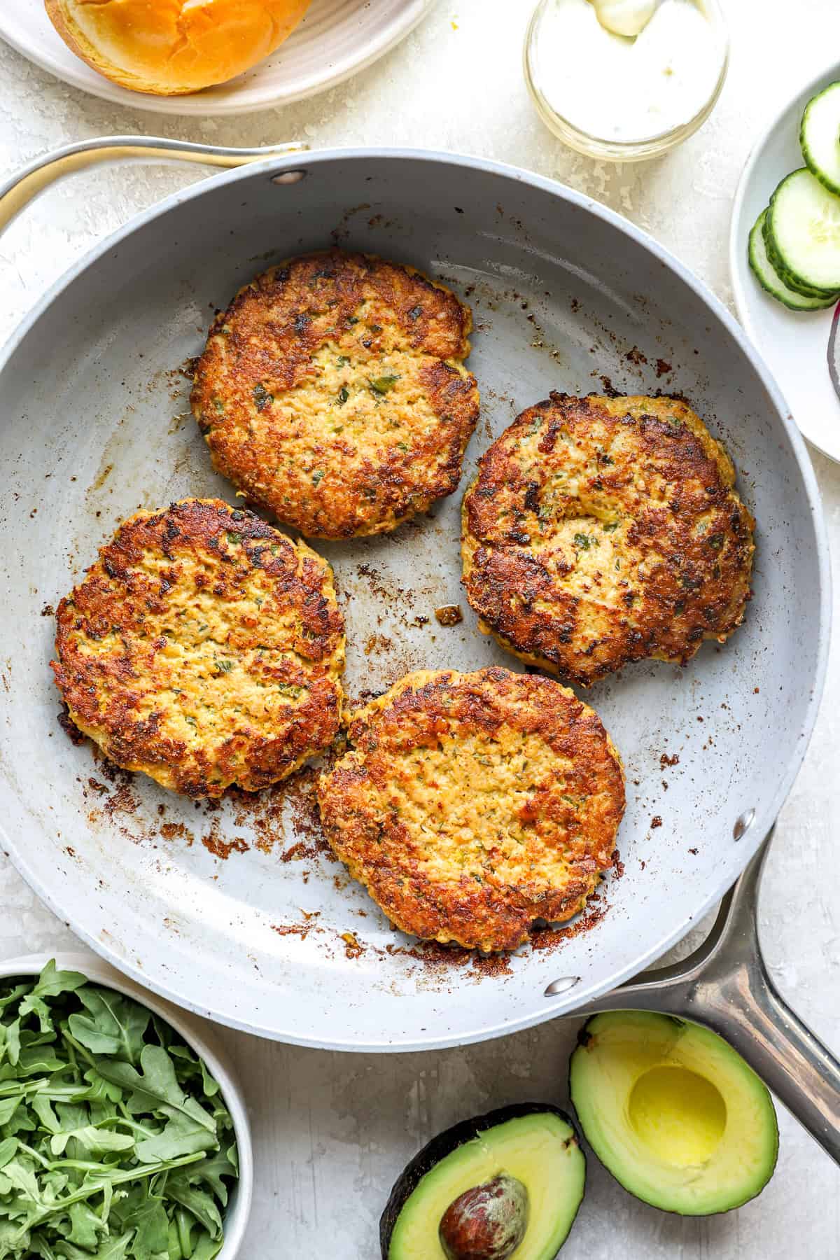 Four ground chicken burgers cooking in a skillet.