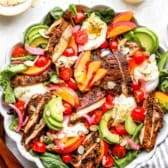 A peach burrata salad topped with chicken.