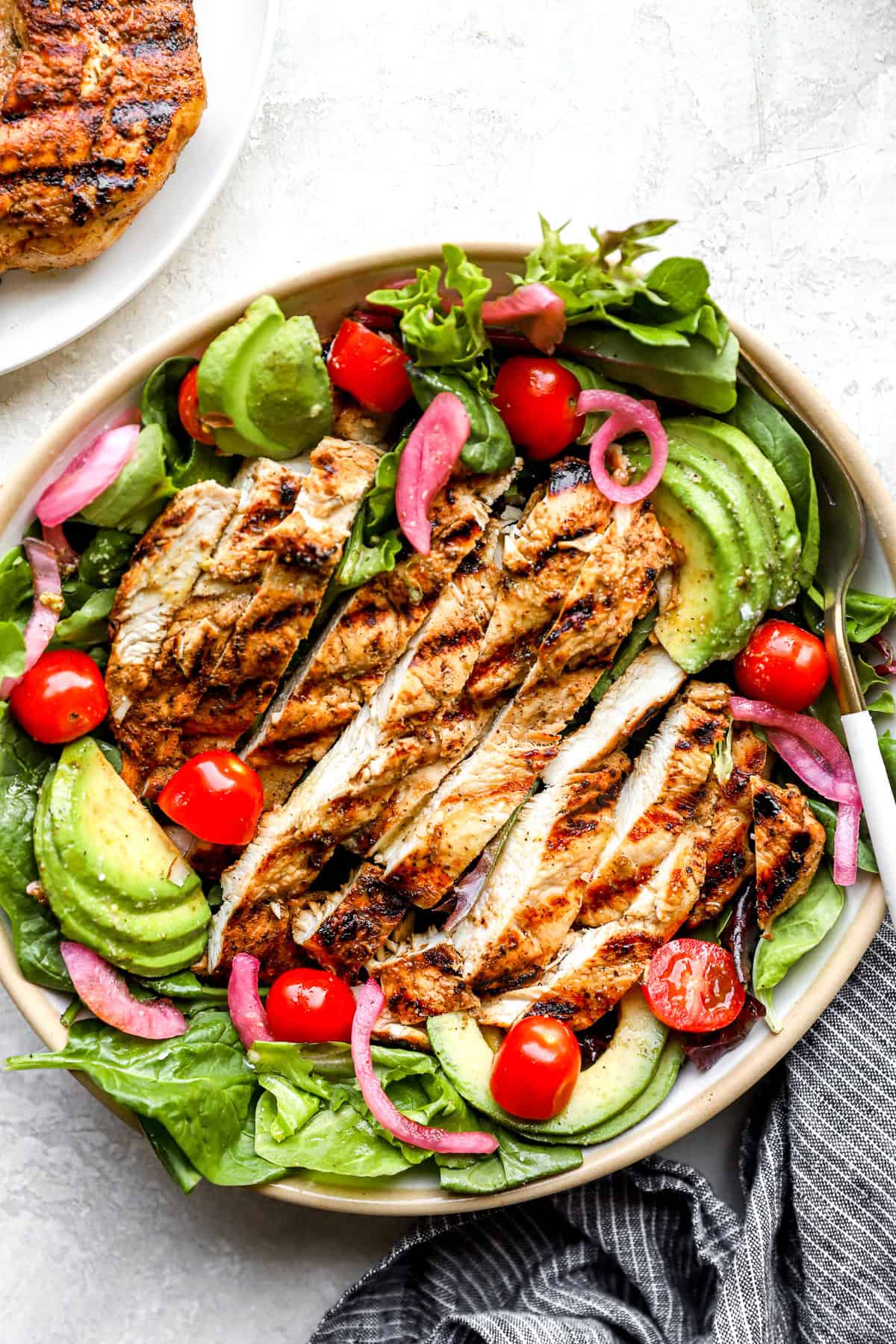 A salad topped with grilled chicken breasts.