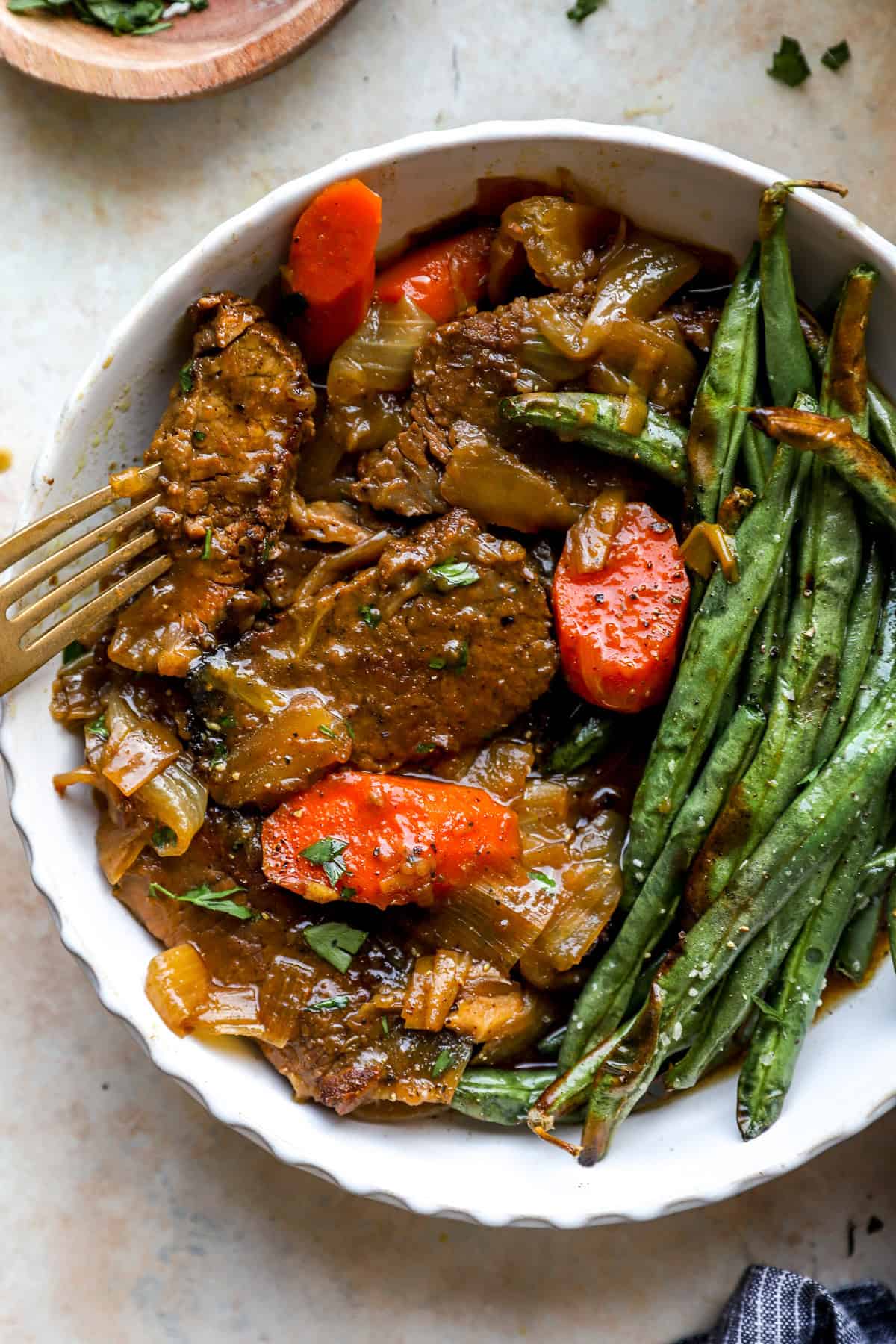 Braised brisket, carrots, and green beans on a plate, a fork on the side.