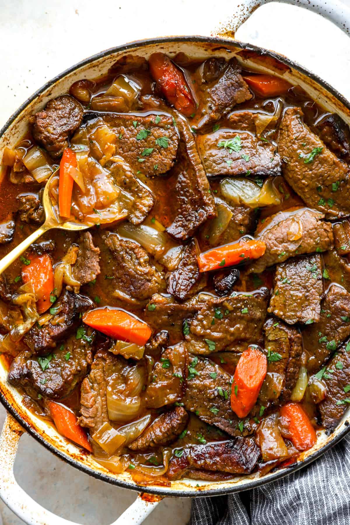 A spoon lifting a scoop of liquid from a pot of braised brisket and veggies.
