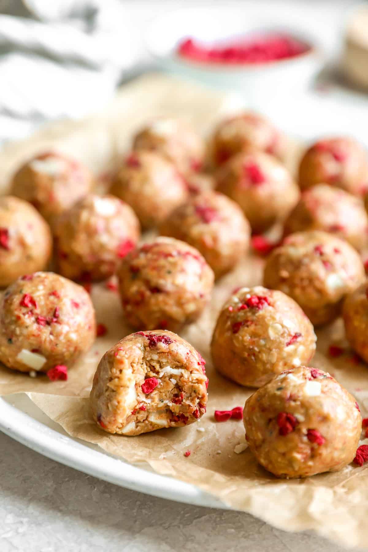 Raspberry white chocolate protein balls on a plate, one missing a bite.