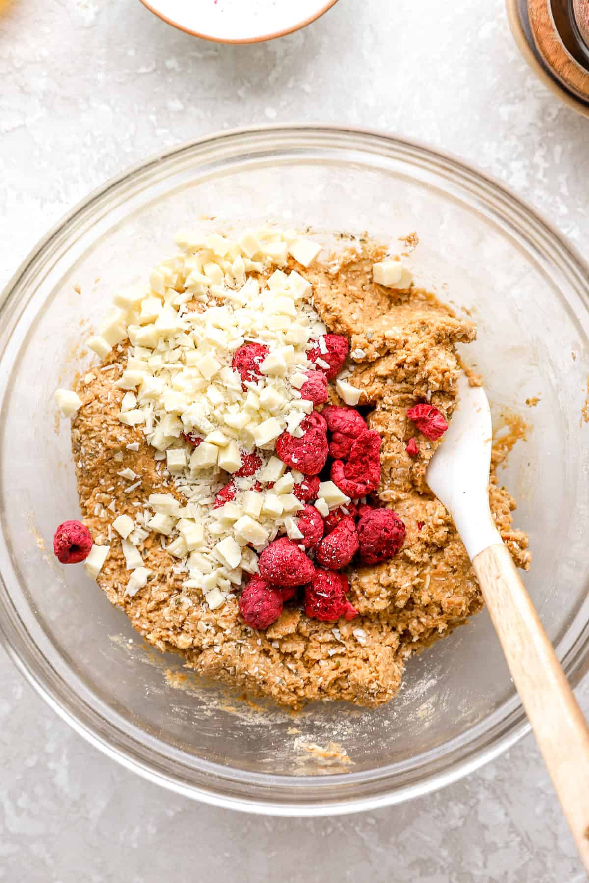 White chocolate chips and freeze-dried raspberries on top of protein ball dough in a bowl.