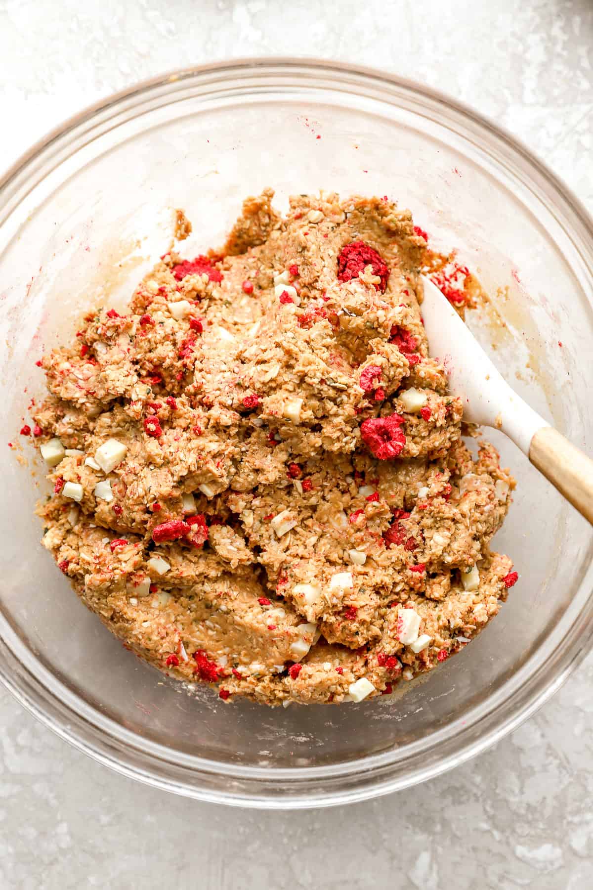 A spatula sticking out of a bowl of raspberry white chocolate protein ball dough.