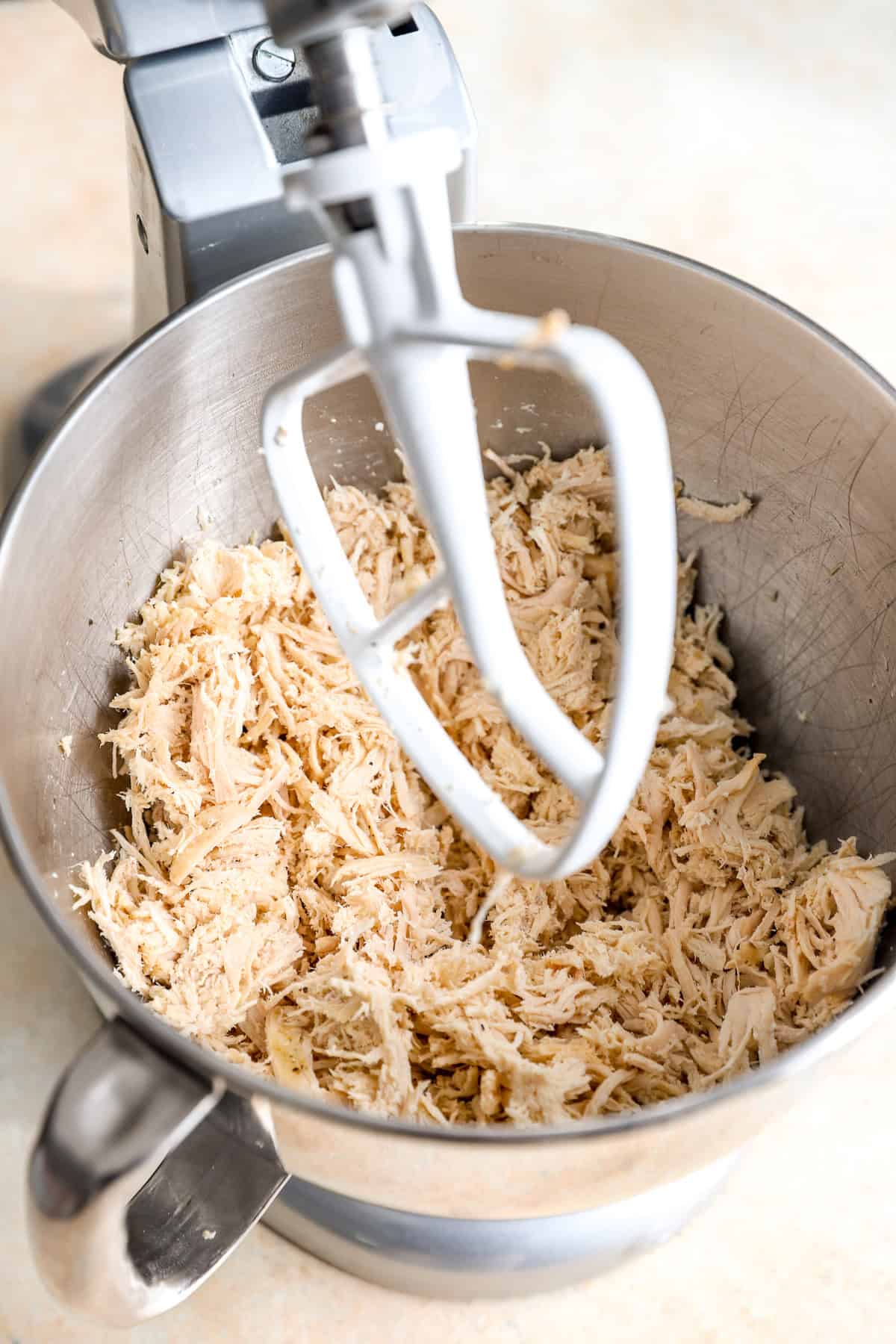 Shredded chicken in the bowl of a stand mixer.
