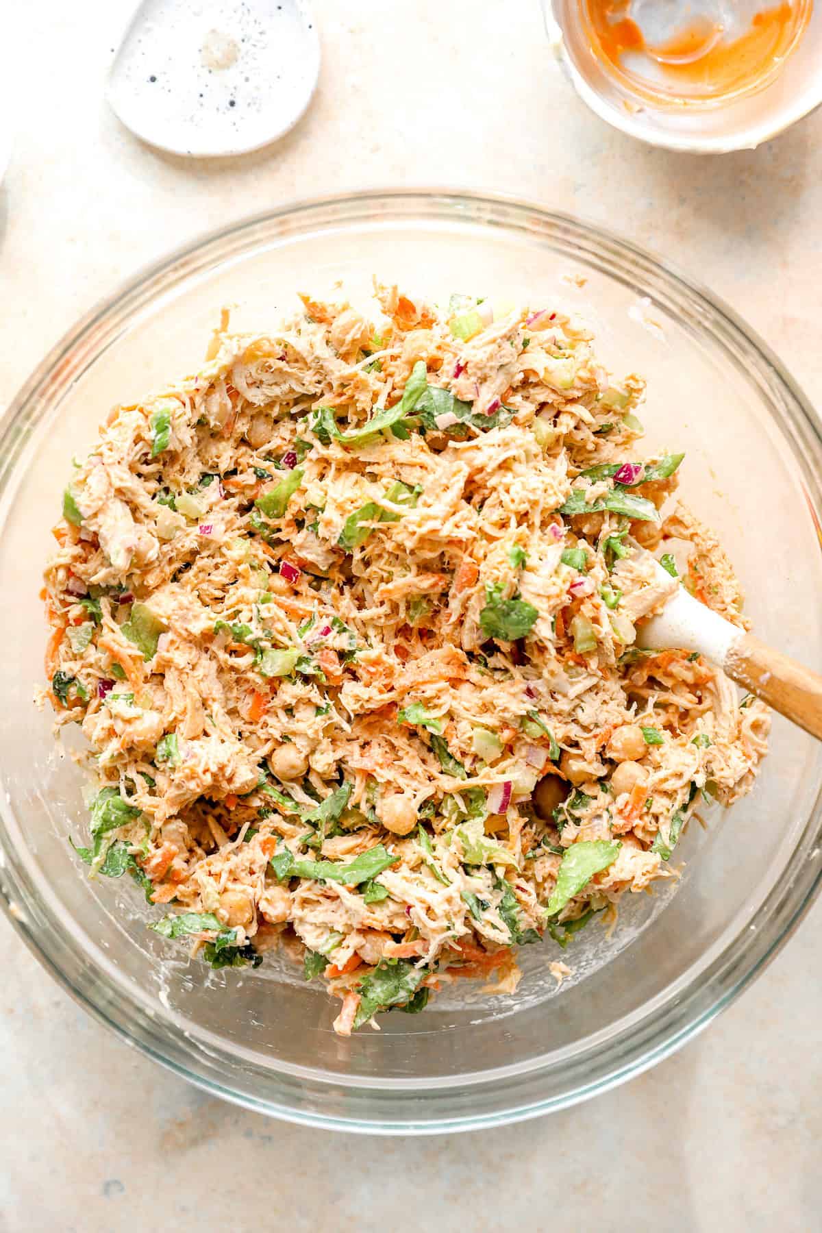 A spoon stirring buffalo chicken salad ingredients in a bowl.