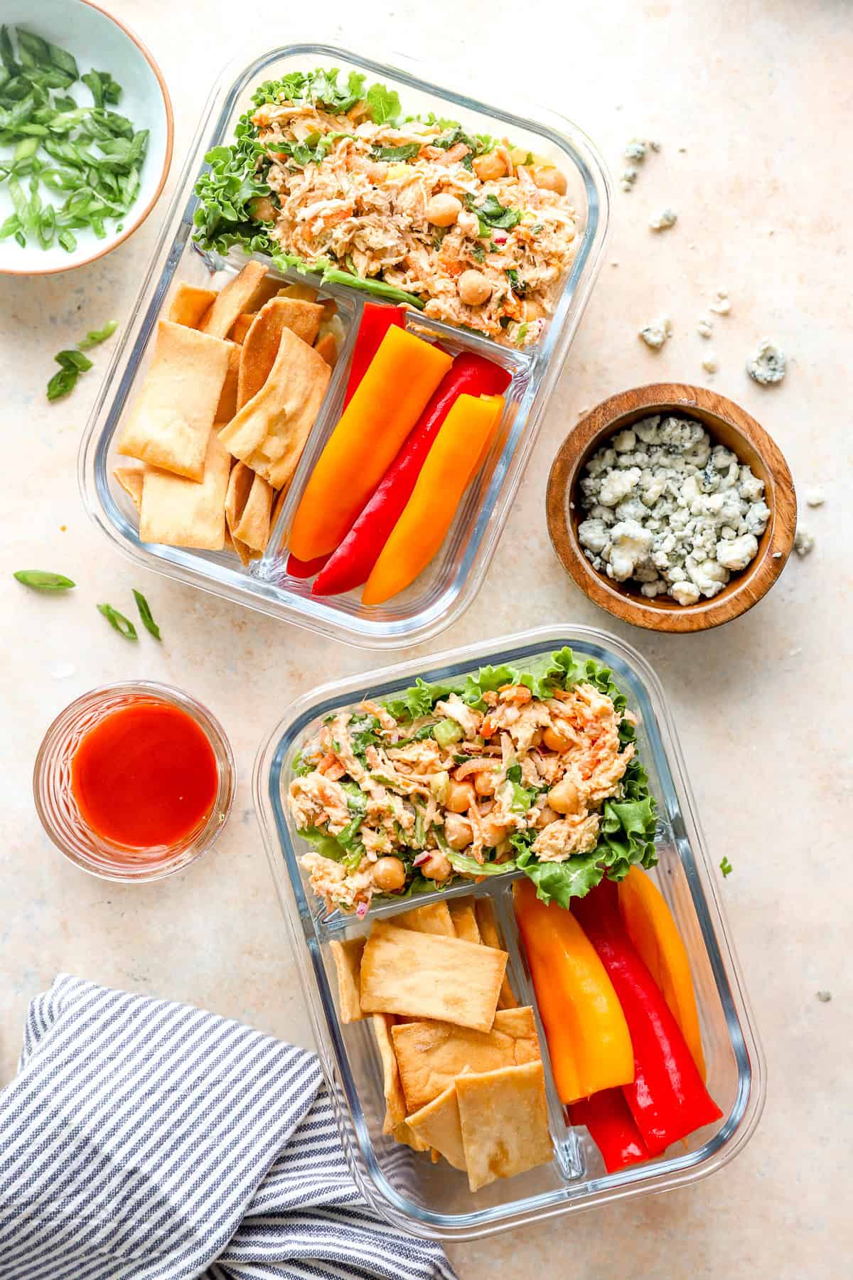 Two lunch boxes with buffalo chicken salad, crackers, and veggie sticks.