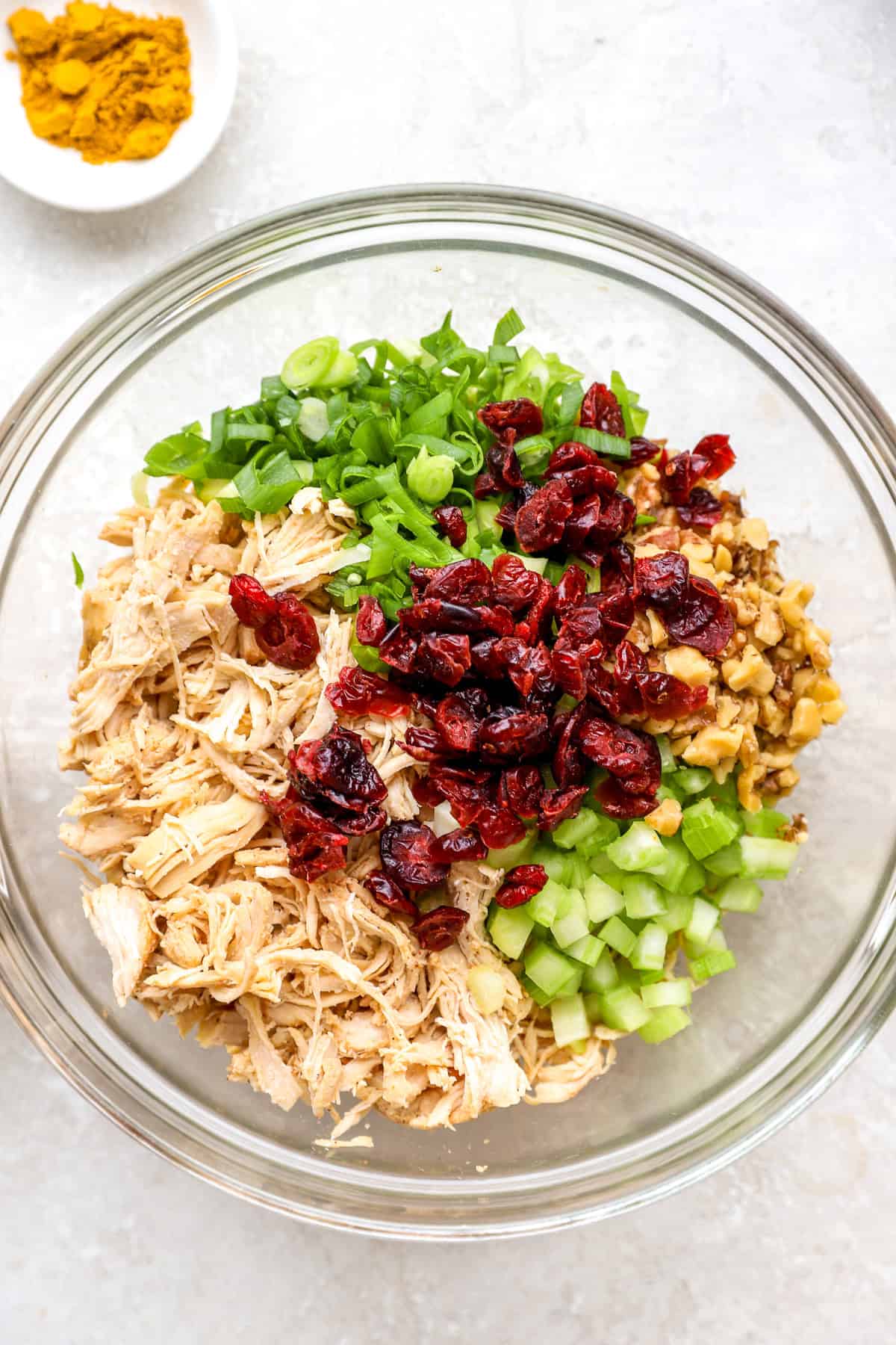 Shredded chicken, walnuts, dried cranberries, shallots, and celery in a bowl.