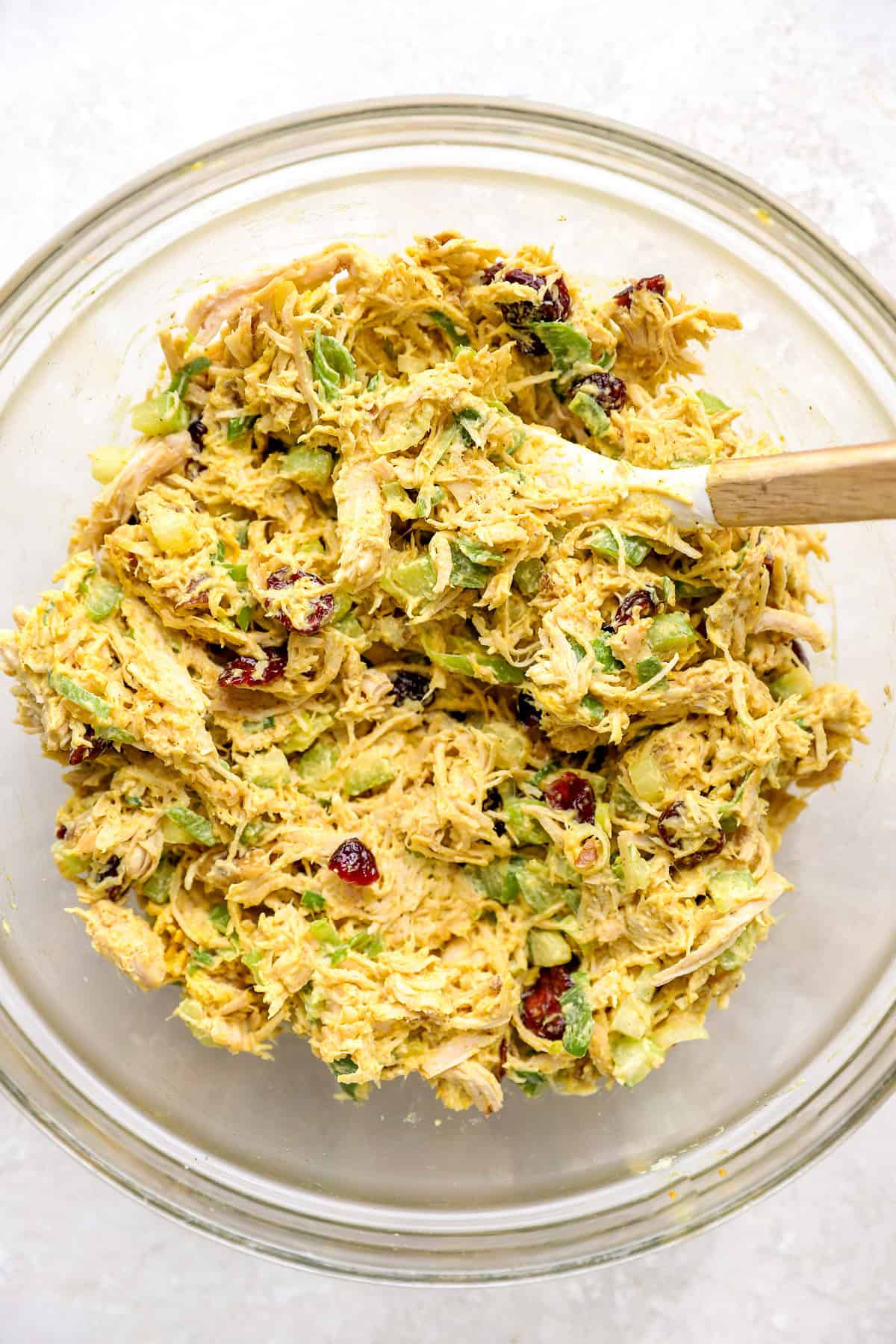 Curried chicken salad being combined in a bowl, a spatula sticking out.