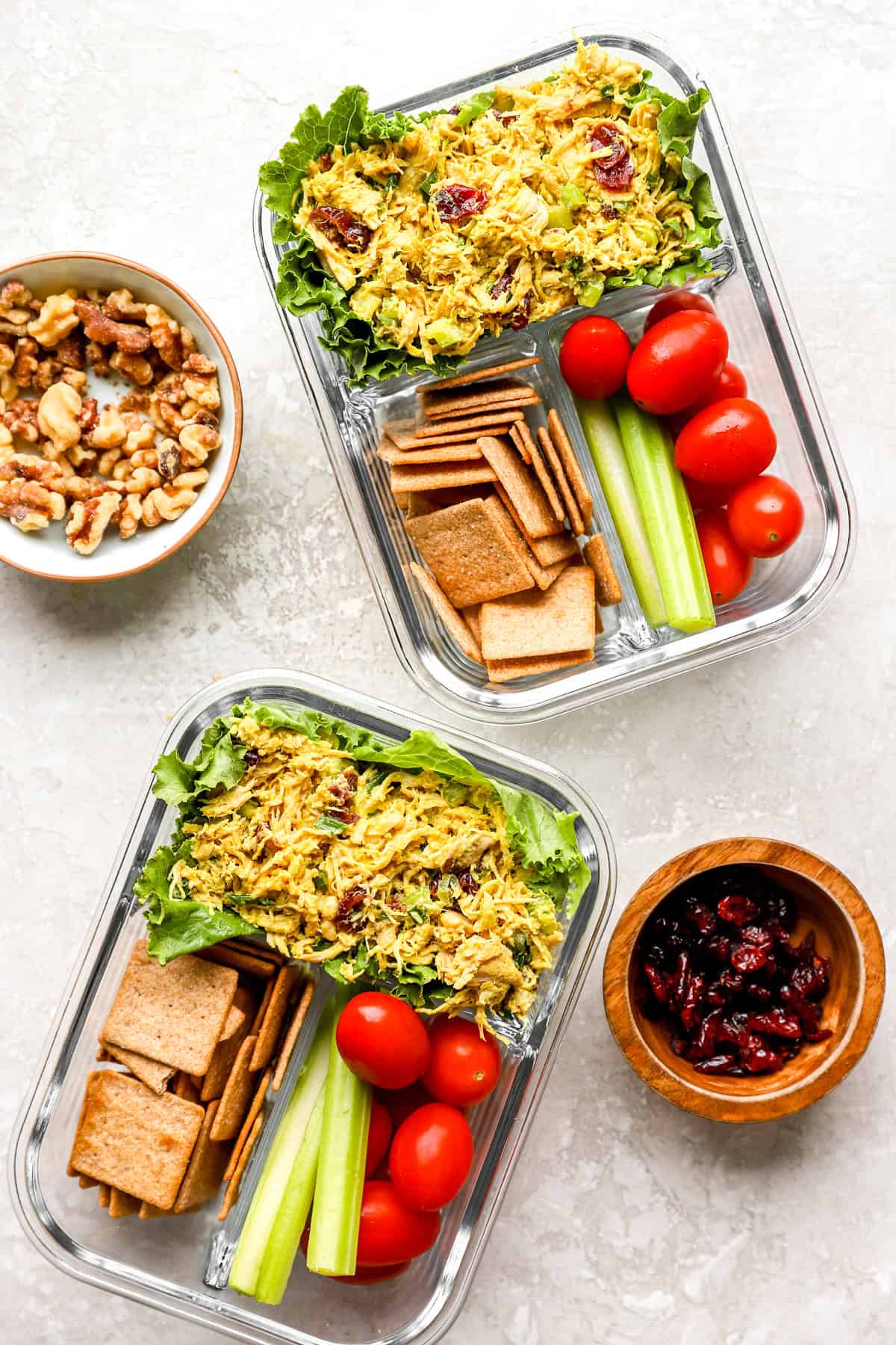Two bento boxes with curried chicken salad, veggies, and crackers.