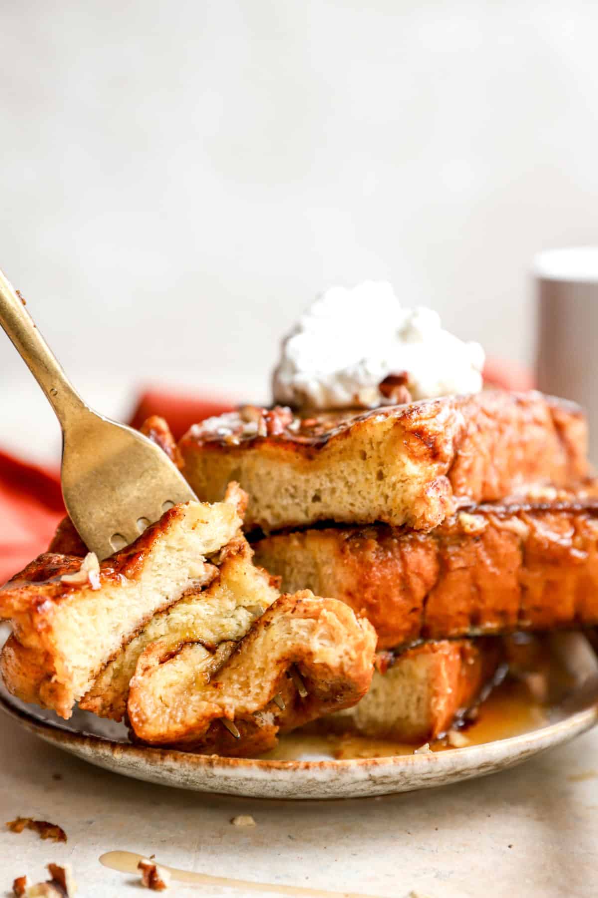 A fork holding a bite of pumpkin French toast next to a stack of French toast on a plate.
